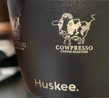 Black Huskee coffee cup with 'Cowpresso Coffee Roasters' logo and 'Huskee' text.